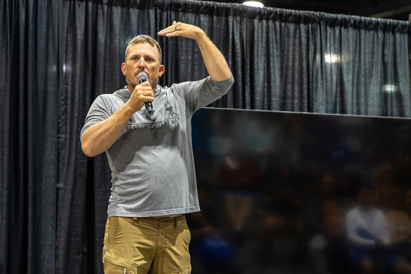 A seminar speaker in a Hunt. Fish. Eat Meat. tee gestures mid-story on stage at the Florida Saltwater Fishing Expo.