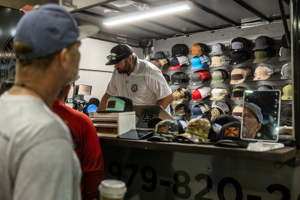 Shoppers wait as a vendor customizes ball caps behind the counter of a hat trailer at the Florida Saltwater Fishing Expo.