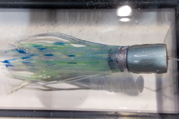 A close-up of a glittering green and blue skirted trolling lure on display at the Florida Saltwater Fishing Expo.