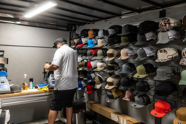 Behind the scenes at a hat customization trailer, rows of trucker caps line the wall at the Florida Saltwater Fishing Expo.