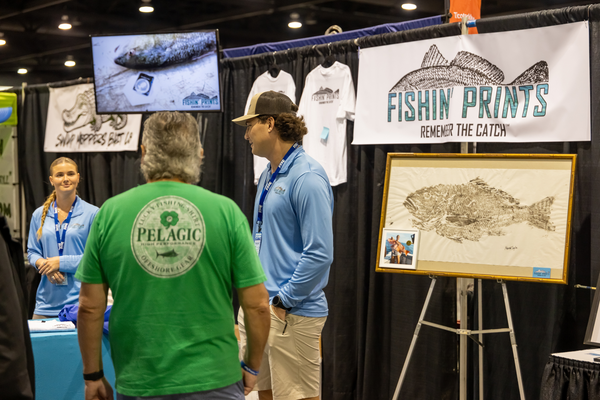 Fishin' Prints staff show off a custom fish print, Remember the Catch, to a visitor at the Florida Saltwater Fishing Expo.
