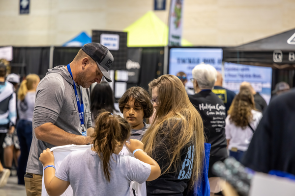 A dad helps his kids into event t-shirts near the Halifax Custom Rod Builders booth at the Florida Saltwater Fishing Expo.