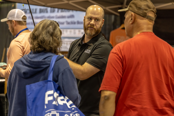 A Blind Cast representative chats with attendees near a tackle ID guide display at the Florida Saltwater Fishing Expo.