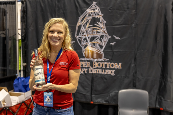 A Copper Bottom Craft Distillery sponsor smiles while holding a bottle of Silver Rum at the Florida Saltwater Fishing Expo.