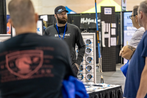A SeaWorx Fishing rep talks with attendees near a display of tackle spools at the Florida Saltwater Fishing Expo.