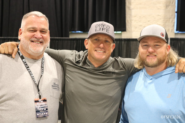 Three staff and guests share a warm, smiling group photo, arms around each other at the Florida Fishing Expo.