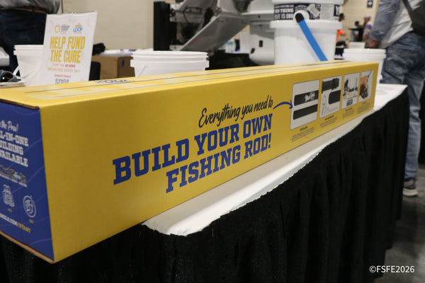 A build-your-own fishing rod kit on display at the Florida Fishing Expo, next to a Help Fund the Cure pediatric cancer charity sign.