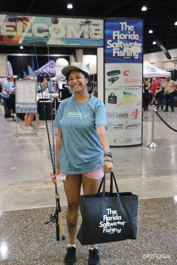 A smiling attendee poses with her rod and a swag bag near the entrance at the Florida Fishing Expo.