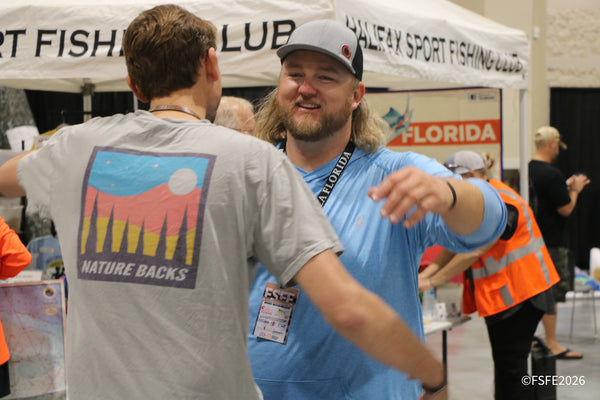 Two grinning anglers share a fist bump near the Halifax Sport Fishing Club booth at the Florida Fishing Expo.