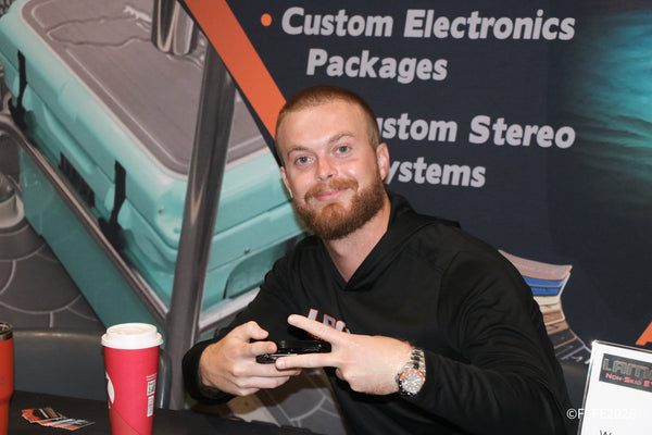 A grinning Lamco Non-Skid rep flashes a peace sign at his custom marine electronics and stereo display at the Florida Fishing Expo.
