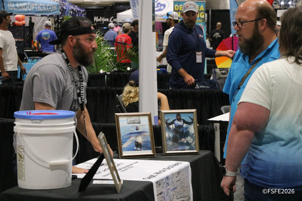 Anglers swap stories over framed catch photos at Capt. Nick Scibilia's booth, with Island Optics visible nearby at the Florida Fishing Expo.