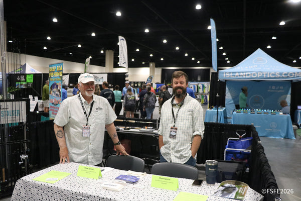 Smiling Spot Stalker Charters staff greet the busy Florida Fishing Expo show floor, with the Island Optics booth glowing behind them.