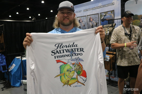 A smiling attendee proudly holds up his Florida Fishing Expo t-shirt featuring a leaping mahi-mahi.