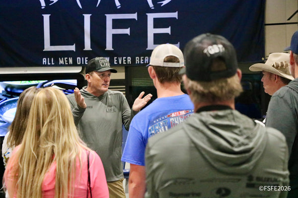 An animated captain gestures while chatting with a small crowd gathered near a boat display at the Florida Fishing Expo.