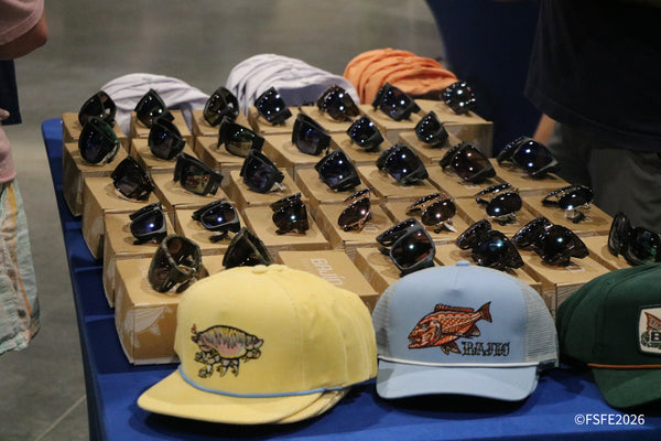 Rows of Bajio sunglasses and fish-embroidered trucker caps fill a vendor table at the Florida Fishing Expo.