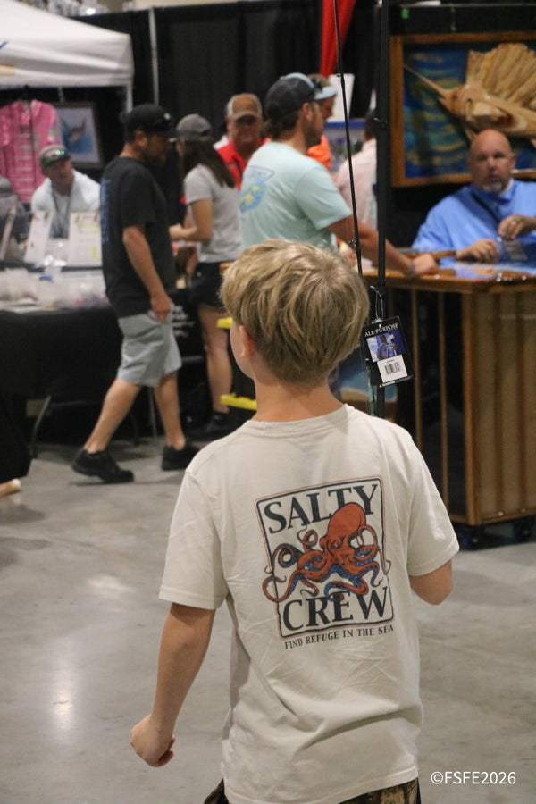 A young angler in a Salty Crew tee weaves through a packed aisle of exhibitor booths at the Florida Fishing Expo.