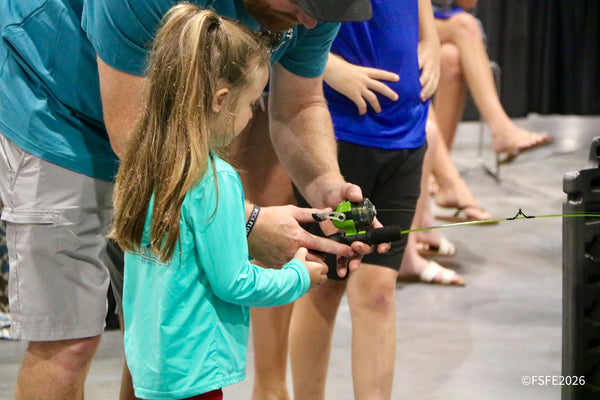 A young angler gets hands-on help casting a rod during a Kids Zone clinic at the Florida Fishing Expo.