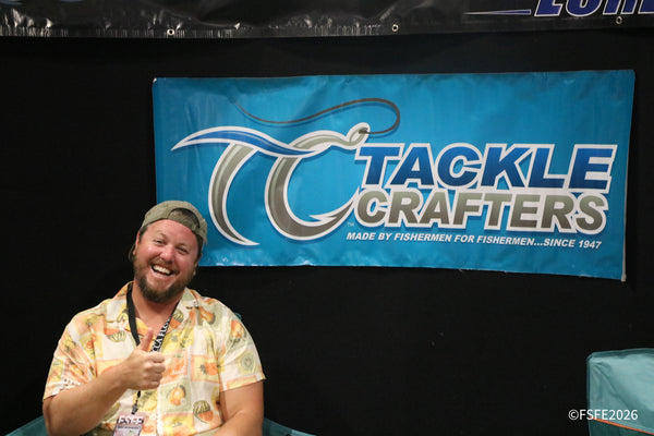 A vendor laughs and gives a thumbs up in front of the Tackle Crafters banner, made by fishermen since 1947, at the Florida Fishing Expo.