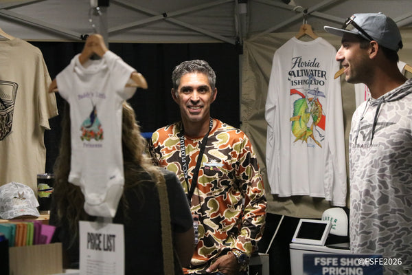 Smiling shoppers browse Florida Saltwater Fishing Expo apparel at a packed merchandise booth.