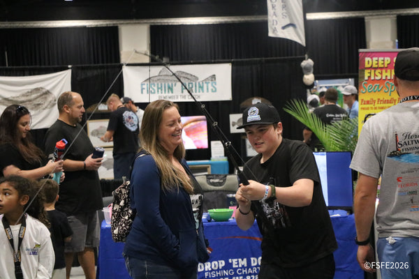 A Fishin' Prints team member smiles as a young angler practices casting near the Drop 'Em Down Fishing Charters booth at the Florida Fishing Expo.