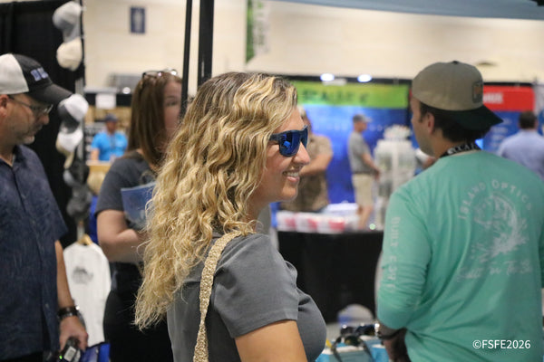 A smiling attendee chats with an Island Optics rep amid a lively crowd at the Florida Fishing Expo.