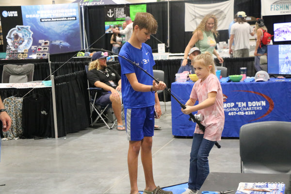 Two young anglers team up on a casting rod in front of the Drop 'Em Down Fishing Charters booth at the Florida Fishing Expo.