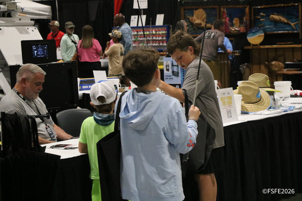 Kids browse a rod rack display amid a busy, crowded aisle of vendor booths at the Florida Fishing Expo.