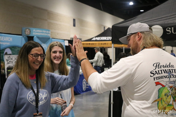 Smiling attendees share a high-five with Florida Fishing Expo staff near the Florida Fish and Wildlife Conservation Commission display.