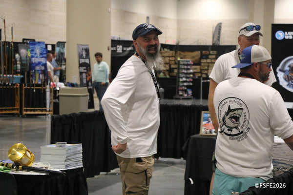 A laughing exhibitor shares a big smile with the NSB Shark Hunters crew nearby at the Florida Fishing Expo.