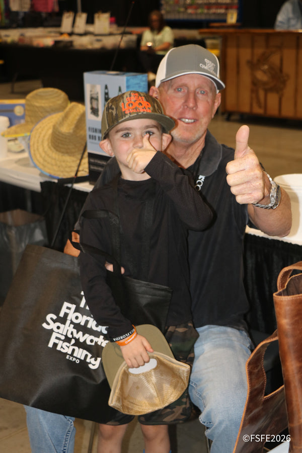 A young angler and his dad flash big thumbs up with their Florida Saltwater Fishing Expo tote bag.