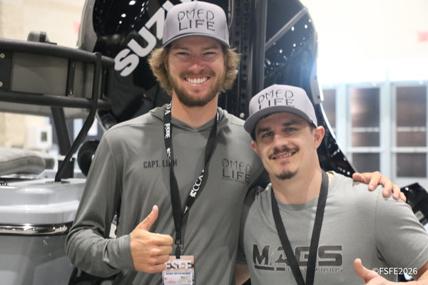 Capt. Liam of DMFD Life gives a big thumbs-up alongside a MAGS Custom Rods rep near a Suzuki outboard at the Florida Fishing Expo.