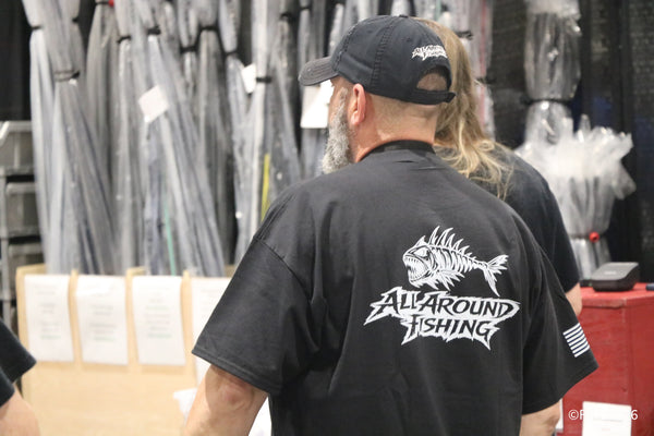 An attendee in an All Around Fishing shirt strolls past racks of rods in the tackle aisles at the Florida Fishing Expo.