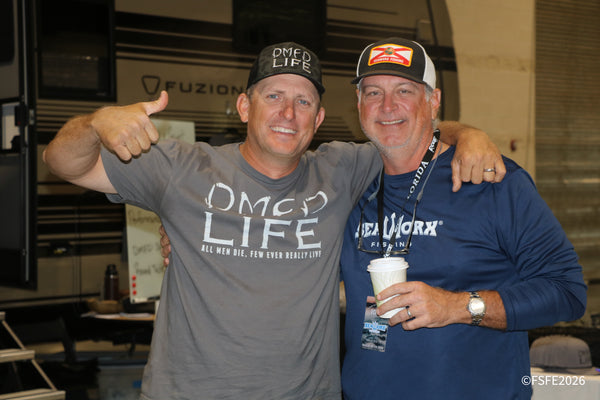 Two grinning vendors from DMFD Life and SeaWorx Fishing pose arm-in-arm at the Florida Fishing Expo.