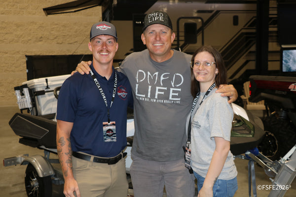 Three smiling vendor staff, including one in a Rapid Rescue Detailing polo, pose together near boat displays at the Florida Fishing Expo.
