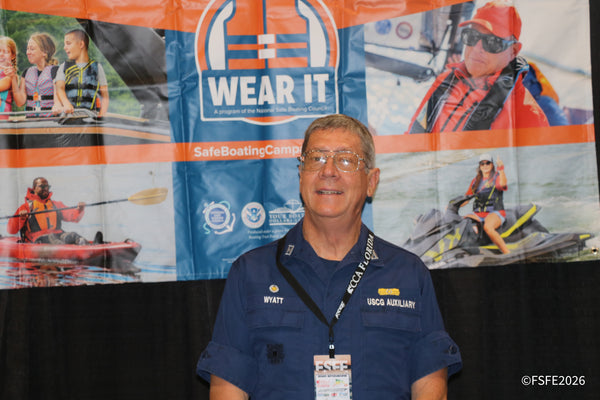 A U.S. Coast Guard Auxiliary volunteer shares boating safety tips in front of the "Wear It" life jacket campaign banner at the Florida Fishing Expo.