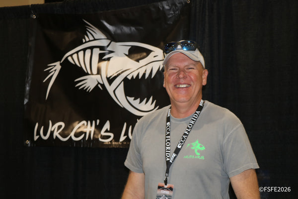 A grinning Lurch's Lures vendor stands in front of his booth banner at the Florida Fishing Expo.