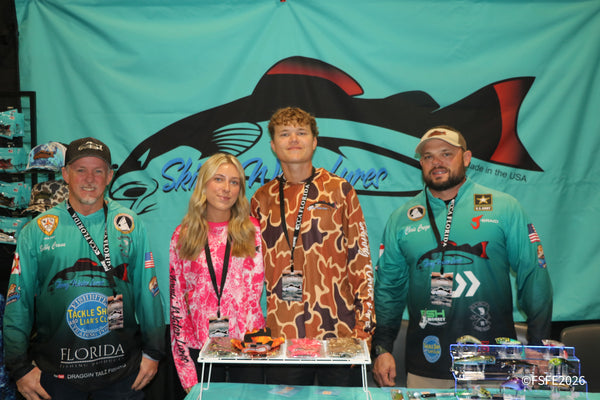 The Skinny Water Lures team of four poses smiling in matching jerseys at their Florida Fishing Expo booth.