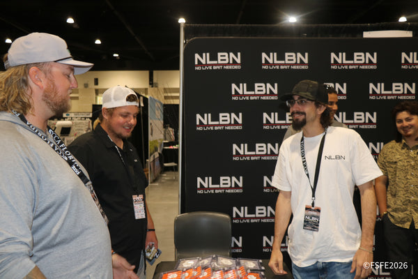 A laughing group gathers in front of the NLBN (No Live Bait Needed) backdrop at the Florida Fishing Expo.