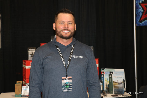 An Outcome Marine Group representative smiles at his Florida Fishing Expo booth, surrounded by marine electronics displays.