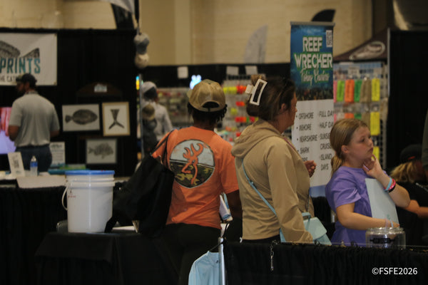 Attendees browse a wall of tackle near the Reef Wrecker Fishing Charters banner at the Florida Fishing Expo.