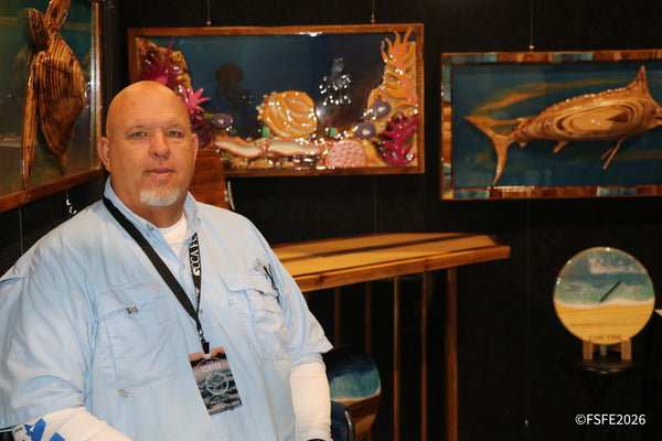 A vendor stands among intricate wooden marine art pieces, including a sailfish and sea turtle, at the Florida Fishing Expo.