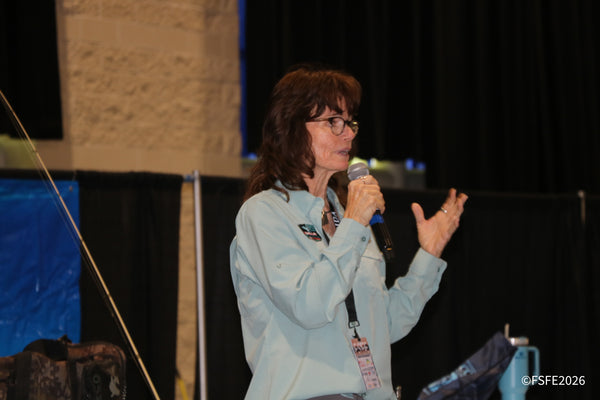A seminar speaker gestures mid-sentence while addressing the crowd with a fishing rod in hand at the Florida Fishing Expo.