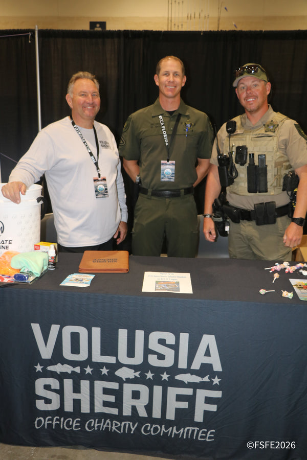 Three smiling members of the Volusia Sheriff's Office Charity Committee staff their booth at the Florida Fishing Expo.