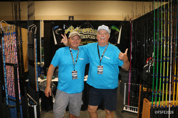 Two beaming Adventurous Custom Rods vendors throw up a peace sign and thumbs-up in their rod-lined booth at the Florida Fishing Expo.