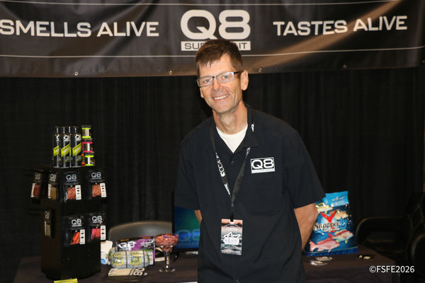 A smiling Q8 Super Bait representative stands beside the brand's scented bait display at the Florida Fishing Expo.