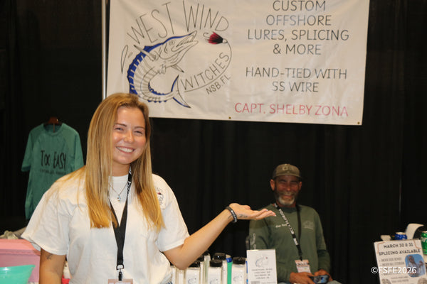 A smiling West Wind Witches vendor gestures toward her custom offshore lures at the Florida Fishing Expo.