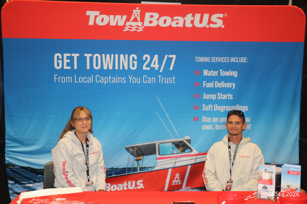 Two friendly TowBoatU.S. representatives smile in front of their 24/7 towing services banner at the Florida Fishing Expo.