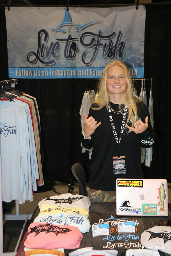 A Live to Fish vendor throws a shaka with a big smile behind her apparel table at the Florida Fishing Expo.