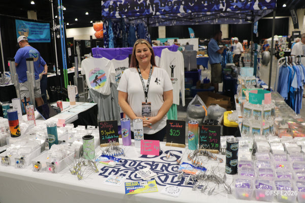 A smiling DS Custom Tackle vendor stands behind a table of rigs, tumblers, and apparel at the Florida Fishing Expo.